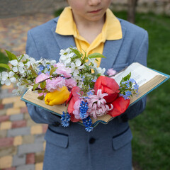 bouquet of spring flowers lie on pages of open book held by child. Time for relaxation and...