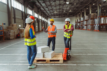 Group of happy managers, workers wearing safety helmet and vest loading boxes on pallet truck