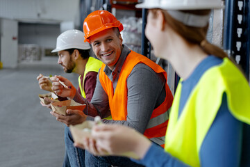 Smiling, worker, engineer wearing hard hat, vest and work wear holding lunch, eating during break