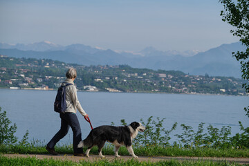Woman with a dog walking in motion in the background Lake Garda, mountain peaks in the snow.