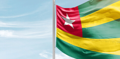 Togo national flag with mast at light blue sky.