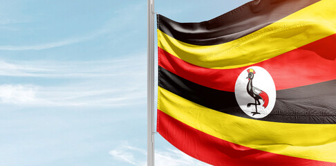 Uganda national flag with mast at light blue sky.