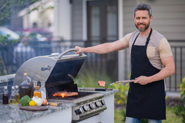Male chef grilling and barbequing in garden. Barbecue outdoor garden party. Handsome man preparing barbecue meat. Concept of eating and cooking outdoor during summer time. - 786934080