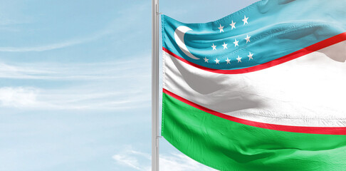 Uzbekistan national flag with mast at light blue sky.