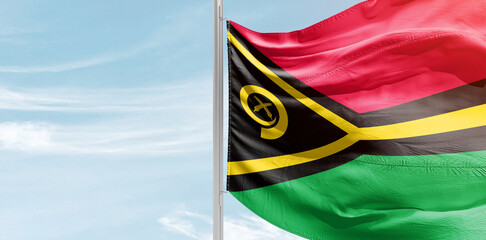 Vanuatu national flag with mast at light blue sky.