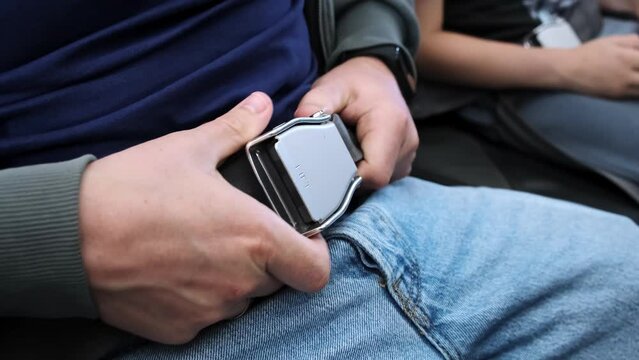 A man passenger fastens himself with a seatbelt on the airplane before takeoff and landing. A person buckles up or lock buckle the seat belt on plane. Concept of safe traveling by air. Safety rules