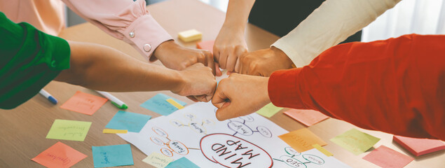 Young happy creative startup group join circle fist bump hands together surrounded by marketing...