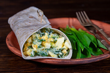 Homemade burrito wraps with boiled eggs, potato, green wild garlic and sour cream for healthy breakfast on plate, closeup - 786946463