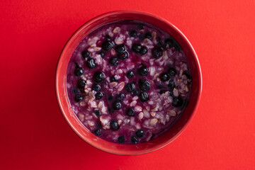 Oatmeal porridge with ripe blueberries for healthy breakfast on red background, closeup, top view - 786946465