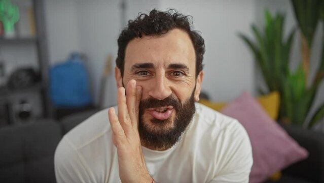 Middle-aged man, handsome with beard, wearing white t-shirt whispering a devious secret, hand covering mouth in indoor chatter. spicy living room talk at home!