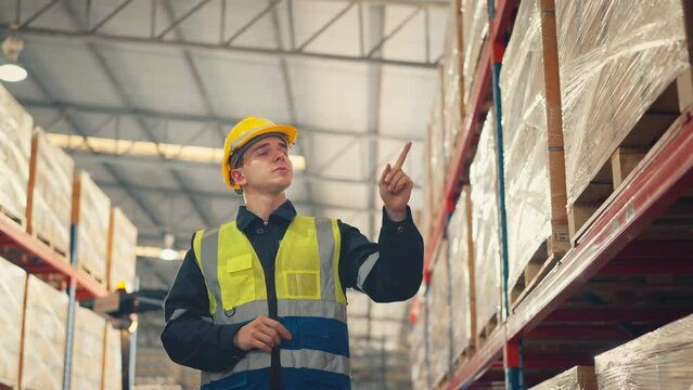 Man worker checks products stock inventory in the retail warehouse full of shelves Male employee wearing hard hat doing work in storehouse.