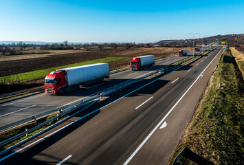 Convoy of red Trucks with white containers on highway, cargo transportation concept in springtime -...