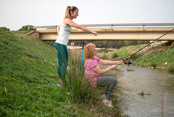 Mother and daughter fishing together by a river while camping in forest