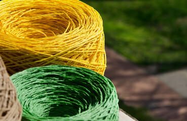 Rolls of yellow and green raffia close-up. Skeins of multi-colored raffia against the background of a green street.