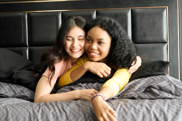 Portraits of two happy young women are lying down on sleeping beds. Two ethnically diverse friends...