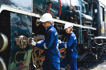 Two men in blue coveralls are working on a train engine. Scene is serious and focused, as the men are likely working on an important task
