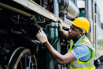 A man in a yellow helmet and safety vest is working on a train engine - obrazy, fototapety, plakaty