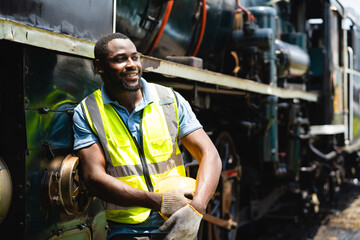 A man in a yellow vest stands next to a train engine. He is smiling and he is happy