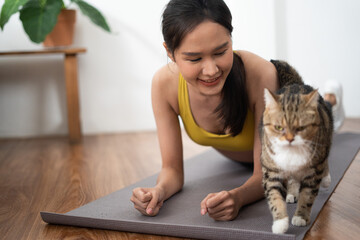 Asian woman exercise training at home doing stretching yoga personal trainer workout in living room indoor on holiday with her cat as good health wellness lifestyle