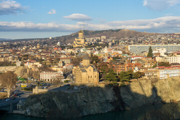 Evening view of Avlabari district of Tbilisi, Georgia from Narikala fortress. A shadow falls on the Mtkvari (Kura) river. Metekhi Church and Trinity Cathedral are visible. - obrazy, fototapety, plakaty