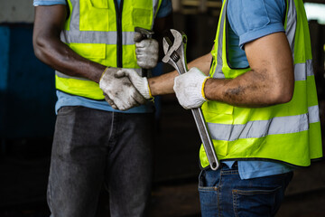 Two men shaking hands while wearing safety gear. One of them is holding a wrench. Concept of...