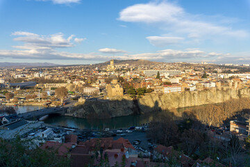 Evening view of Avlabari district of Tbilisi, Georgia from Narikala fortress. A shadow falls on the Mtkvari (Kura) river. Metekhi Church and Trinity Cathedral are visible. - obrazy, fototapety, plakaty