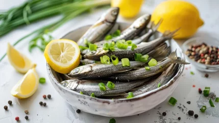 Foto op Aluminium Fresh sprats with green onion spices and lemon slices on a white table in a close up shot © 2rogan