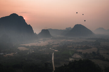 A sunset view of mountains and silhouettes of hot air balloons