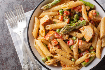 Creamy chipotle chicken penne pasta with asparagus, peppers, green peas, onion and garlic close-up...