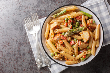 Hot chicken pasta with asparagus, bell peppers and green peas in a creamy chipotle cheese sauce closeup in the bowl on the table. Horizontal top view from above - obrazy, fototapety, plakaty