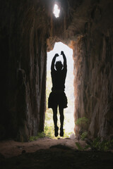 A silhouette of a man jumps in the entrance to a cave