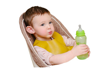 Happy toddler baby drinking from a bottle while sitting on a high chair, isolated on white background. The child boy in the bib has lunch in the home kitchen. Kid aged one year six months
