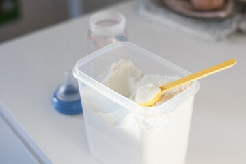 Dry powder formula milk for feeding babies in a can with yellow plastic scoop and empty feeding bottle