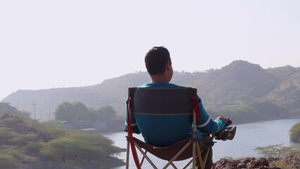 isolated man sitting at camping chair at mountain top with lake view at morning