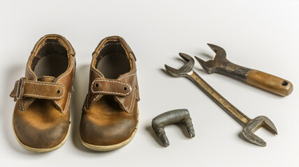 Child's brown leather shoes with a pipe wrench and bent pipe fitting on a white surface.