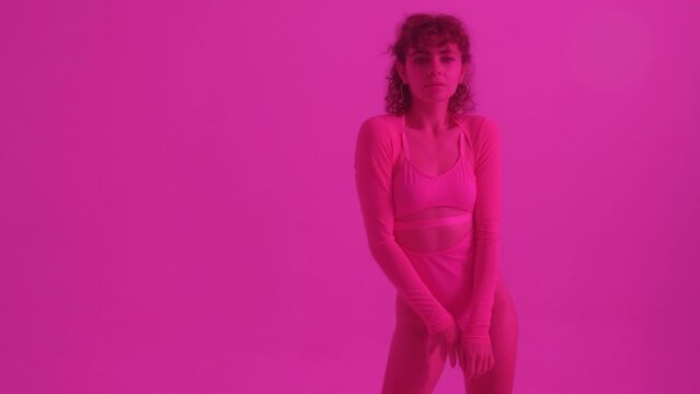 Beautiful girl in a pink swimsuit on a pink background in the style of the 80s. Doing fitness.
