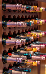 Champagne or cava bottles of different metallic colored labels lined up and stacked on wooden shelves of a wine rack in a gourmet liquor store from a luxury private collection.