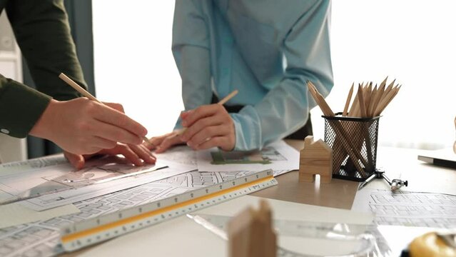 Smart architect and safety engineer discussion about building blueprint on table with architectural document, measurement tools and wooden block scatter around at modern office. Closeup. Delineation.