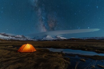 Illuminated orange tent under a starry sky in a snowy mountain landscape
