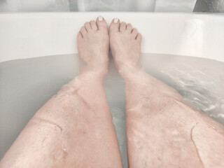 Legs during Relaxing Bath Time in a Tranquil Home Bathroom. Person enjoys a moment of relaxation, with their legs extended in bathtub filled with water, invoking serene atmosphere in a cozy bathroom