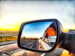 The side mirror of the car and the sun with bright rays behind it and the track on a trip in nature - obrazy, fototapety, plakaty