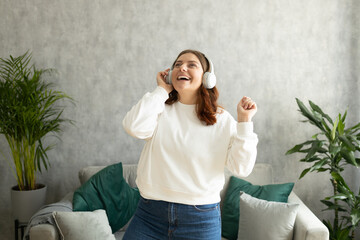 Happy 30s woman singing and dancing in living room at home. Independent female portrait. Alone at...