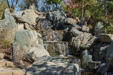 Krasnodar "Japanese Garden". Cascading waterfall with many steps. Artificial stone bed of artificial river against a blurred background of greenery. Selective focus. Park "Krasnodar" or Galitsky Park
