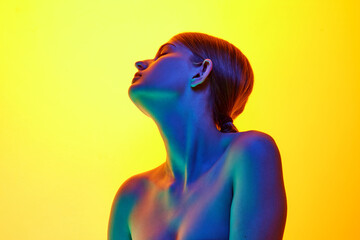 Slender, tender lady with bare shoulders posing in mixed neon light against gradient studio background. Concept of natural beauty, organic cosmetic, spa procedures, face-care.