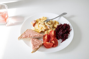 Delicious food - omelette with sausage, tomato slices, slices of bread with capelin caviar  and red beet on a white plate.