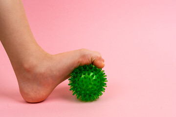 green needle ball for massage and physical therapy on a pink background with a child's foot, the...