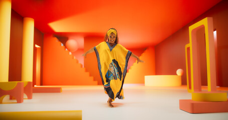 Beautiful Black Woman in African Outfit Dancing Energetically in Geometric Abstract Orange Environment. Creative Female Performing Modern Dance Choreography in a Studio While Looking at the Camera