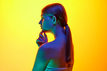 Portrait of young woman posing looking away with thoughtful expression in neon light against gradient studio background. Concept of natural beauty, organic cosmetic, spa procedures, face-care.