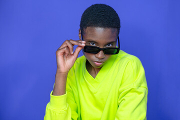 Fashion black model with sunglasses posing with attitude on blue studio background. High quality photo