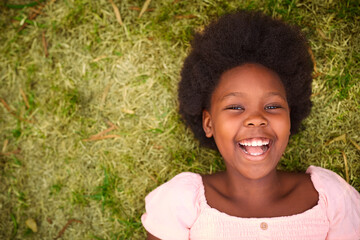 Looking Down On Smiling And Laughing Young Girl Outdoors Lying On Grass In Garden Or Countryside